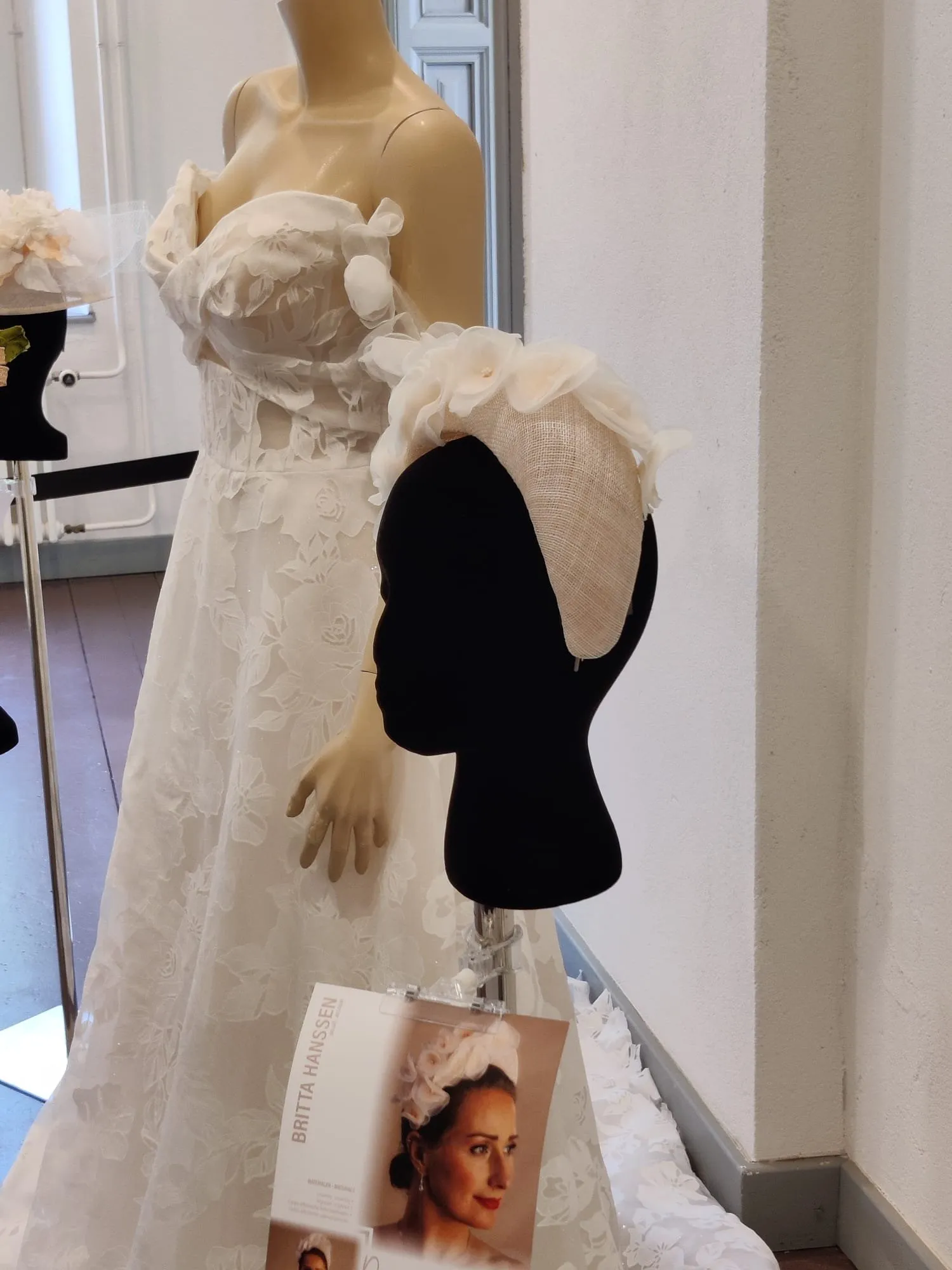 Roomkleurig bruidshoofdstuk in sinamay met organza bloemen, bij een kanten trouwjurk