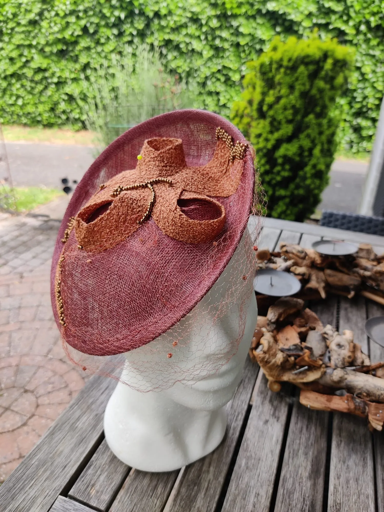 Bordeauxrode fascinator met koperkleurige strik en fijne voilette