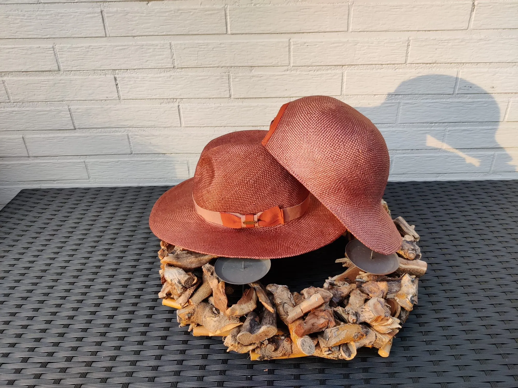 Twee terracottakleurige strohoeden, een fedora en een model met ronde rand