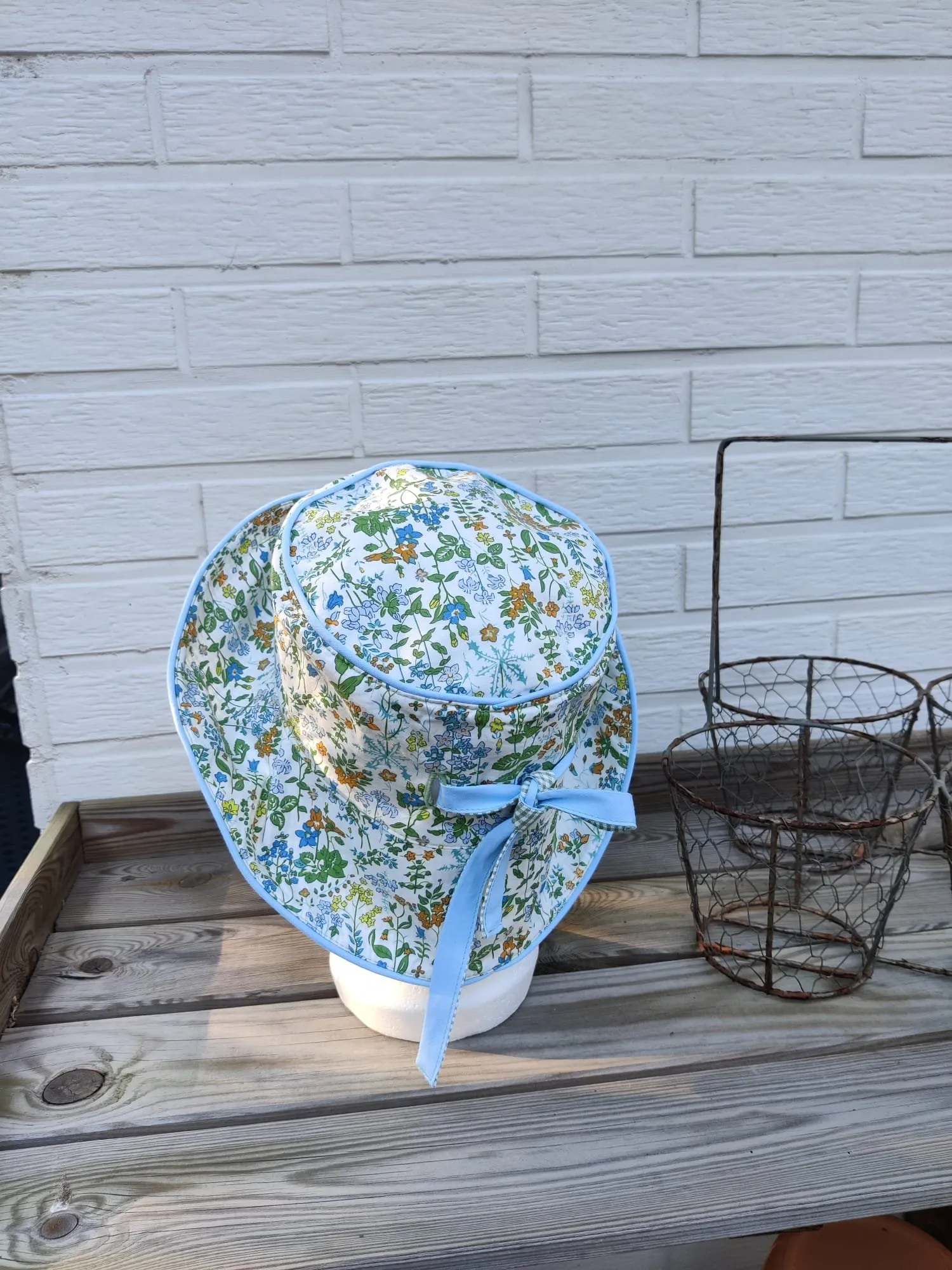 Buckethoed met fijne bloemenprint in blauw, groen en oker, met lichtblauwe biesrand