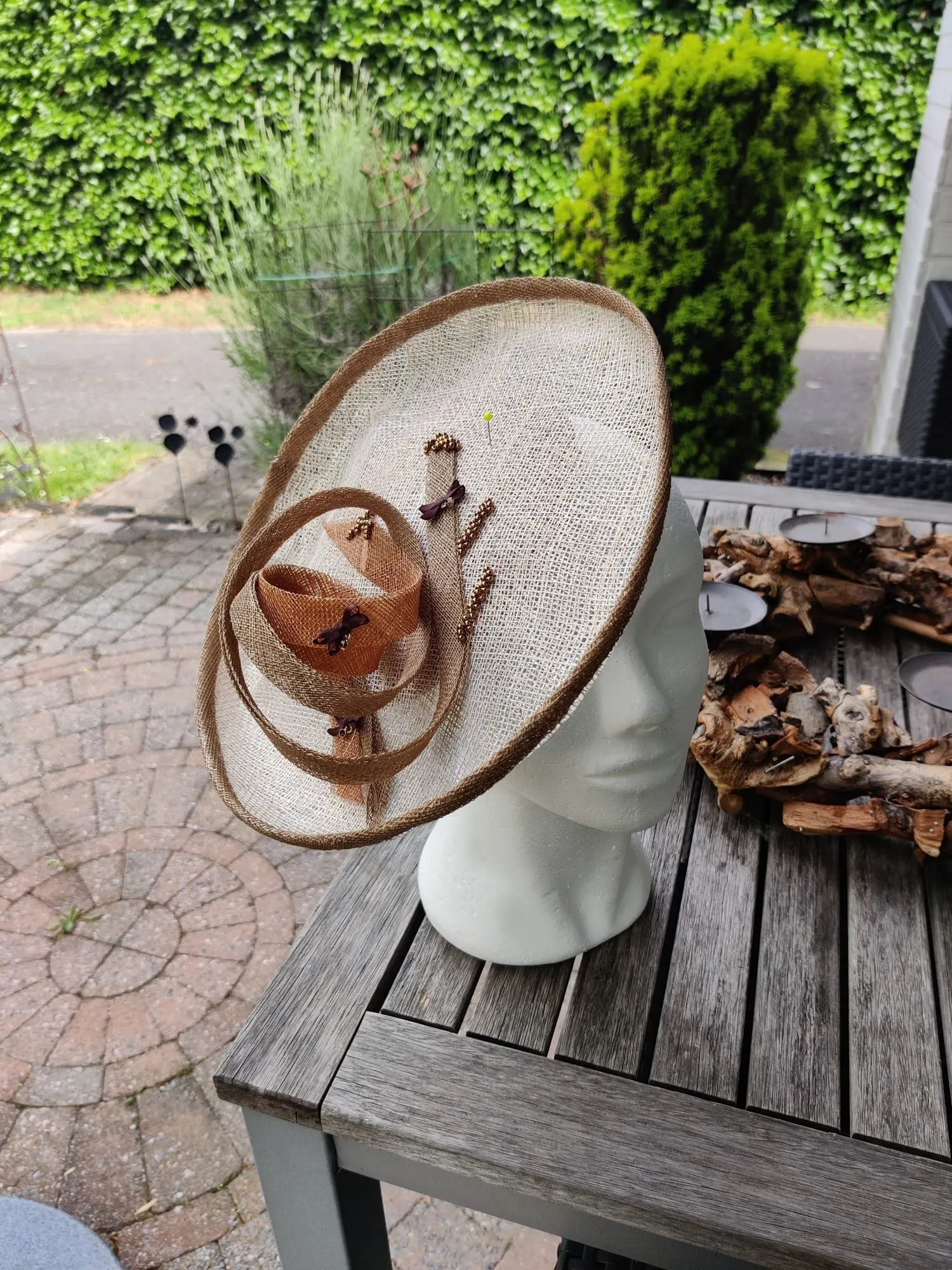 Brede sinamay schotelhoed in naturel met koperen strik en kraaltjes