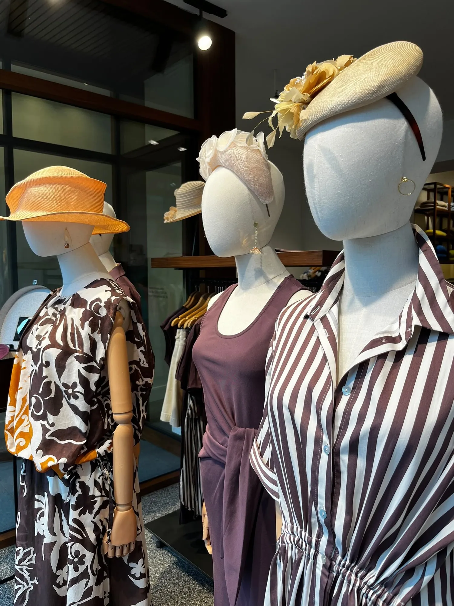 Etalage met hoeden op paspoppen tussen de kleding
